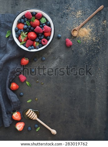 Berry frame with copy space on right. Strawberries, raspberries, blueberries and mint leaves, honey, cane sugar, dark grunge background, top view, copy space