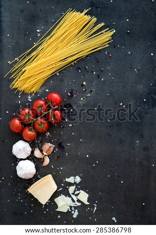 Food frame. Pasta ingredients. Cherry-tomatoes, spaghetti pasta, garlic, basil, parmesan and spices on dark grunge backdrop, copy space, top view