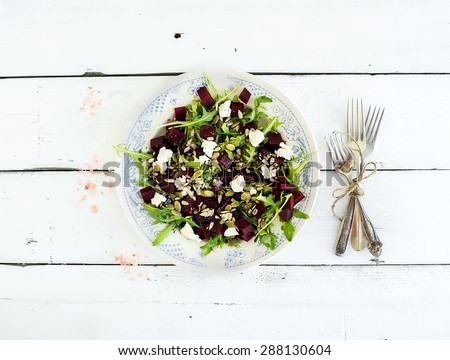Beetroot salad with arugula, feta cheese and pumpkin seeds in vintage plate over white rustic wooden background, top view