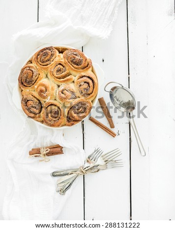 Freshly baked cinnamon buns in a dish on a rustic white wooden table, top view