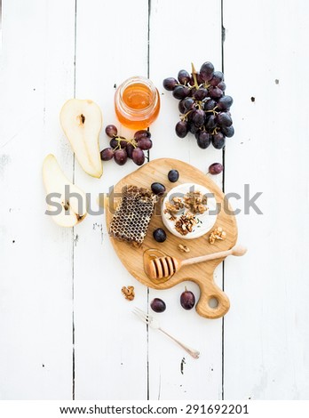Camembert cheese with grape, walnuts, pear and honey on oak serving board over white rustic wood backdrop, top view copy space