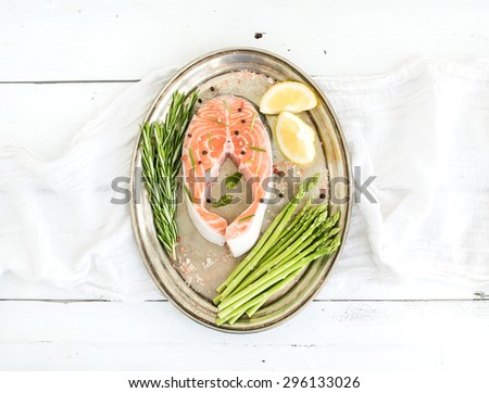 Raw salmon steak with asparagus, lemon, spices and rosemary on vintage silver tray over white wooden backdrop, top view
