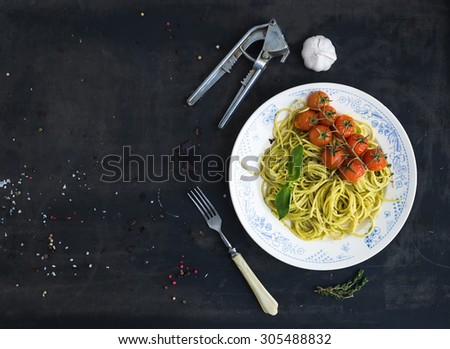 Pasta spaghetti with pesto sauce, basil, garlic, baked cherry-tomatoes on grunge dark table, top view, copy space