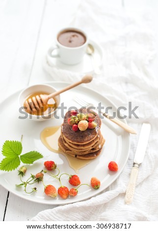 Breakfast set. Buckwheat pancakes with fresh garden strawberries, honey and cup of coffee over white wooden backdrop