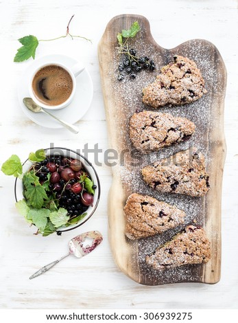 Fresh black-currant scones with coffee and bowl of berries over rustic walnut wood serving board, top view, copy space