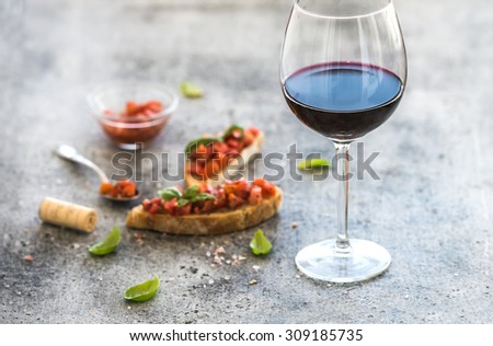 Wine appetizer set. Glass of red wine, brushettas with fresh tomato and basil on over rustic grunge grey backdrop