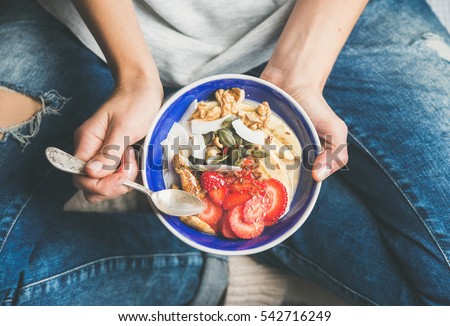Eating healthy breakfast bowl. Yogurt, granola, seeds, fresh and dry fruits and honey in blue ceramic bowl in woman' s hands. Clean eating, dieting, detox, vegetarian food concept ストックフォト © 