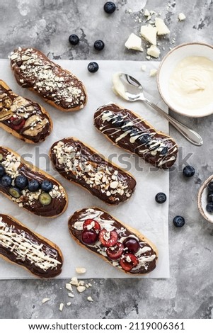 Eclairs with chocolate topping, nuts and berries. Chocolate, nut, banana, cherry and blueberry eclairs. Dessert on a plate. Top view ストックフォト © 