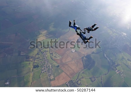 Three skydivers in freefall with sun lighting up the earth below through the clouds
