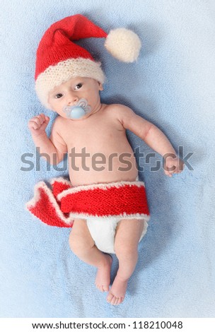Fashion photo of a cute baby with funny knitted hat (Santa\'s hat) for cold weather lying on a blue background.