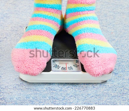 Overweight woman in funny socks standing on a retro style weighing machine.