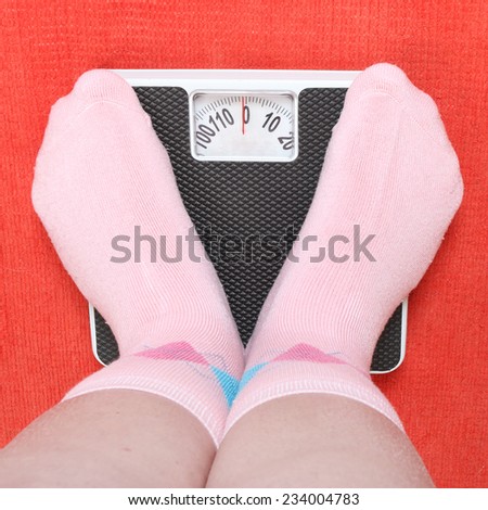 Overweight woman in funny socks standing on a weighing machine.