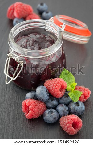 Raspberry and bilberry jam in a jar and fresh berries on the table
