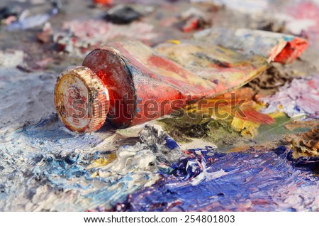 Closeup of old oil paint tube with red colour lying on dirty artistic palette ,background for creative art design