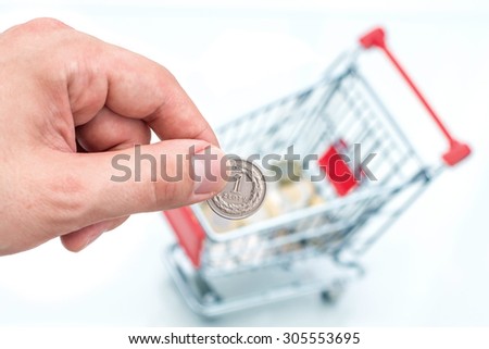 Male hand throws a coin into money box of the shape of trolley. The conception of how to cost-effective spend money while shopping.
