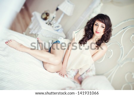 Beautiful brunette woman in the bedroom sitting on the bed. Sleep, morning awakening.