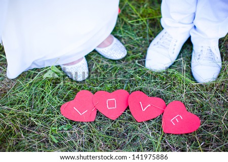 The word love written on the hearts lying on the grass on a background of the feet of the bride and groom.