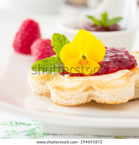 Breakfast: crispy toast in flower shape with butter and raspberry jam. Decorated with yellow pansy flower and mint leaf. Selective focus.
