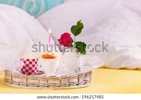 Birthday breakfast in bed. With little cupcake, burning candle and pink rose in eggshell. Selective focus.