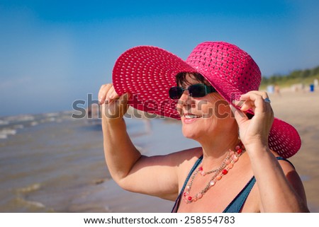Happy mature woman with pink hat on the beach. Selective focus.