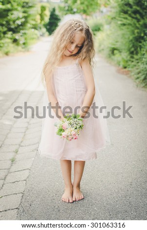 little shy girl in pale pink dress with flowers in her hands and cute crown on her head. selective focus