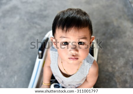 Asian baby boy looking up and feeling need help , stand on mini car