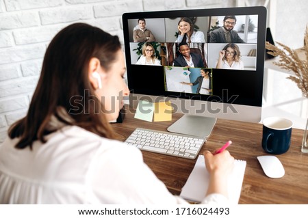 Online training. The back view of a girl who learns online by video conference online. On the screen, the teacher tells the information to her and other participants in the conference