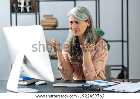 Confused gray-haired mature lady, business woman manager or consultant, looking at the computer in confusion, received an incomprehensible message, or strange news
