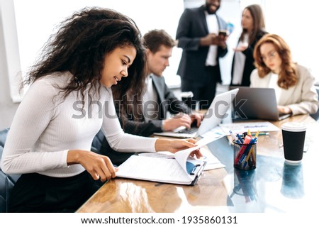 Concentrated african american woman doing paperwork, sitting in modern office on conference. Focused business lady learning financial graphs, working on corporate project at briefing meeting