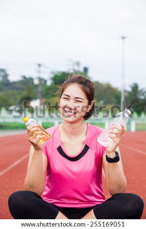 female runner smiling with hand holding energy drink and water