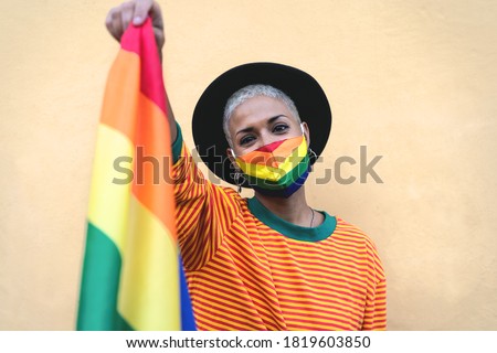 Young woman wearing gay pride mask holding rainbow flag symbol of Lgbtq social movement