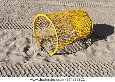 yellow metal trash can on a clean sand beach on a sunny day
