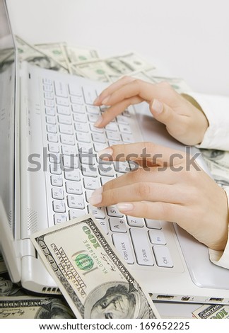 Profitable job: Female hands typing on white laptop keyboard with lot dollar banknotes (big earnings)