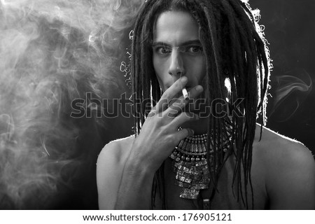 Young man\'s portrait. Stylish handsome guy with dreadlocks and a cigarette and a variety of stylish silver jewelry dreadlocks and  - Close-up face