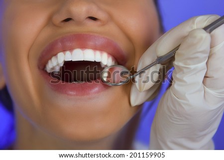 Close-up of female patient having her teeth examined by dentist, visit to the dentist, oral checkup with mirror on a blue background