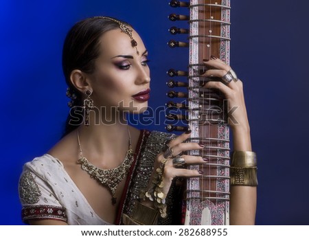 Beautiful Young Indian Woman in Traditional Sari Clothing with oriental jewelry, Bridal Makeup Playing the Sitar. Beautiful Bollywood Girl. Eastern fairy tale  (blue lens effect)
