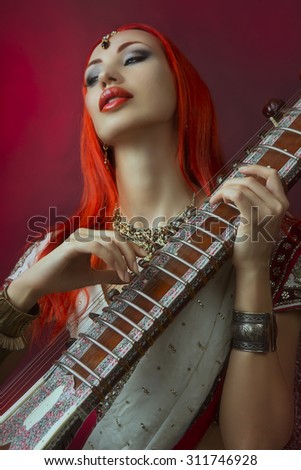 Beautiful Young Redhead Sexy Woman in Traditional Indian Sari Clothing with Oriental Jewelry and Bridal Makeup Playing Raga the Sitar. Beautiful hot Bollywood Girl. Eastern Music