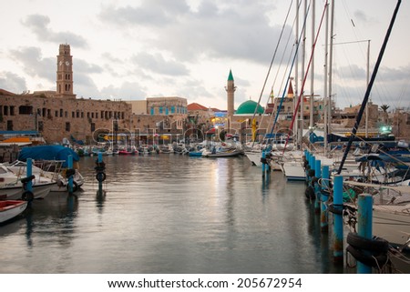 ACRE, ISRAEL - JULY 17, 2014: Local fishing boats, yachts with and nearby monuments, at sunset in the fishing harbor in the old city of Acre, Israel. Acre was a major harbor city for many centuries