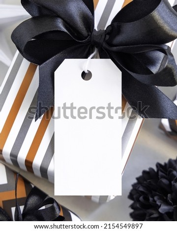 Present with vertical blank gift tag and black bow close up. Gift boxes wrapped in Striped geometric paper near black and white decor. Christmas, New Year, Birthday, Anniversary label mockup Stock foto © 