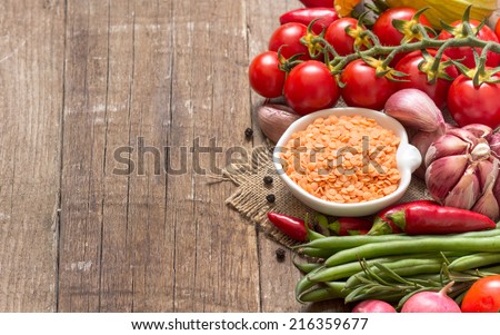 Red lentils in bowl and vegetables on a wooden table
