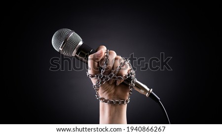 World press freedom day concept. Hand holding a microphone with chain on dark background, symbol of press freedom or speech freedom.