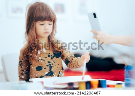 
Mother Taking a Photo of Her Daughter Painting. Proud mom photographing her child while drawing 
