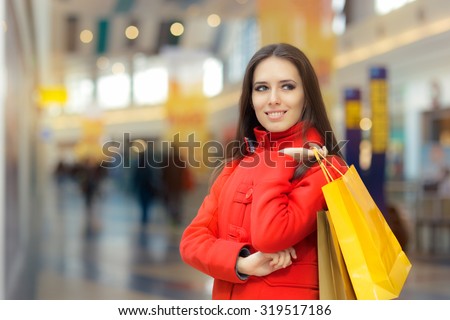 Happy Girl in a Red Coat Shopping in a Mall - Smiling fashion woman holding shopping bags in a big mall