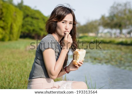 portrait asia Young girl happy and eat bread for picnic resting at outdoor garden