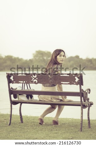 woman sitting and smile on bench facing to the natural lake with retro filter
