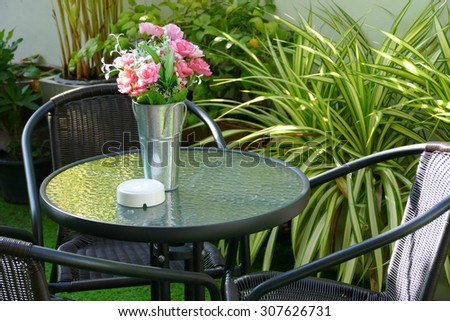 black rattan chair, desk and fake pink rose in the vase at the patio