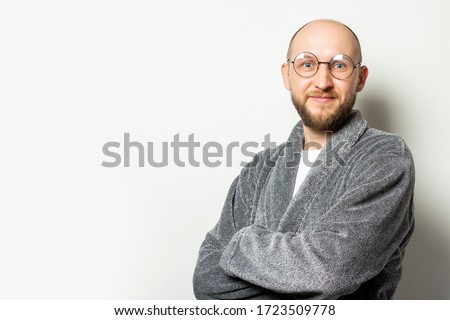 Portrait of a young bald man with a beard in a dressing gown and glasses with arms crossed on his chest on an isolated light background. Emotional face Stock foto © 