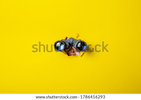 Female hand holds black binoculars on a yellow background. Journey, find and search concept