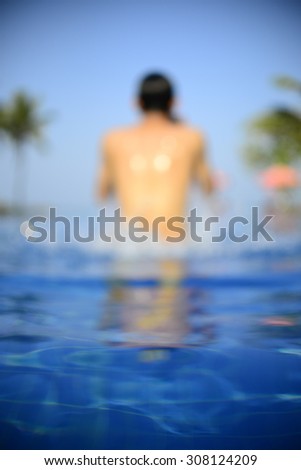 vignette photo of a back shot of a blurred male in the swimming pool with blue water-a perfect holiday concept
