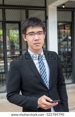 business man concept photo, young and handsome asian business man wearing glasses holding a phone in his hand looking forward  (selective focus technique applied)